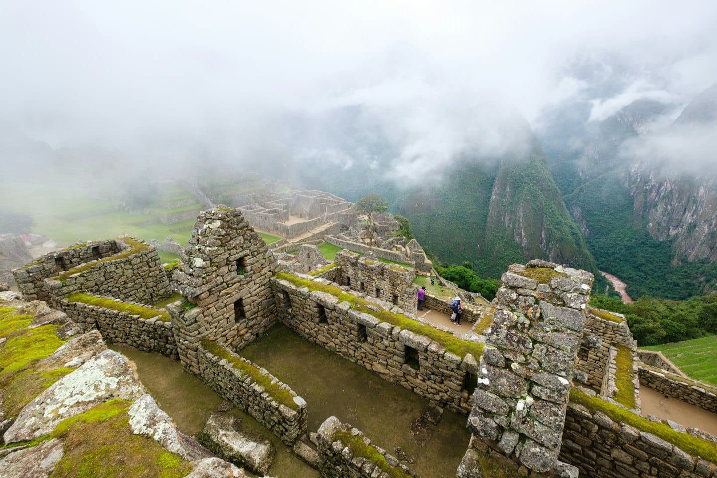 Machu Picchu ruins shrouded in mist with green mountains and river.