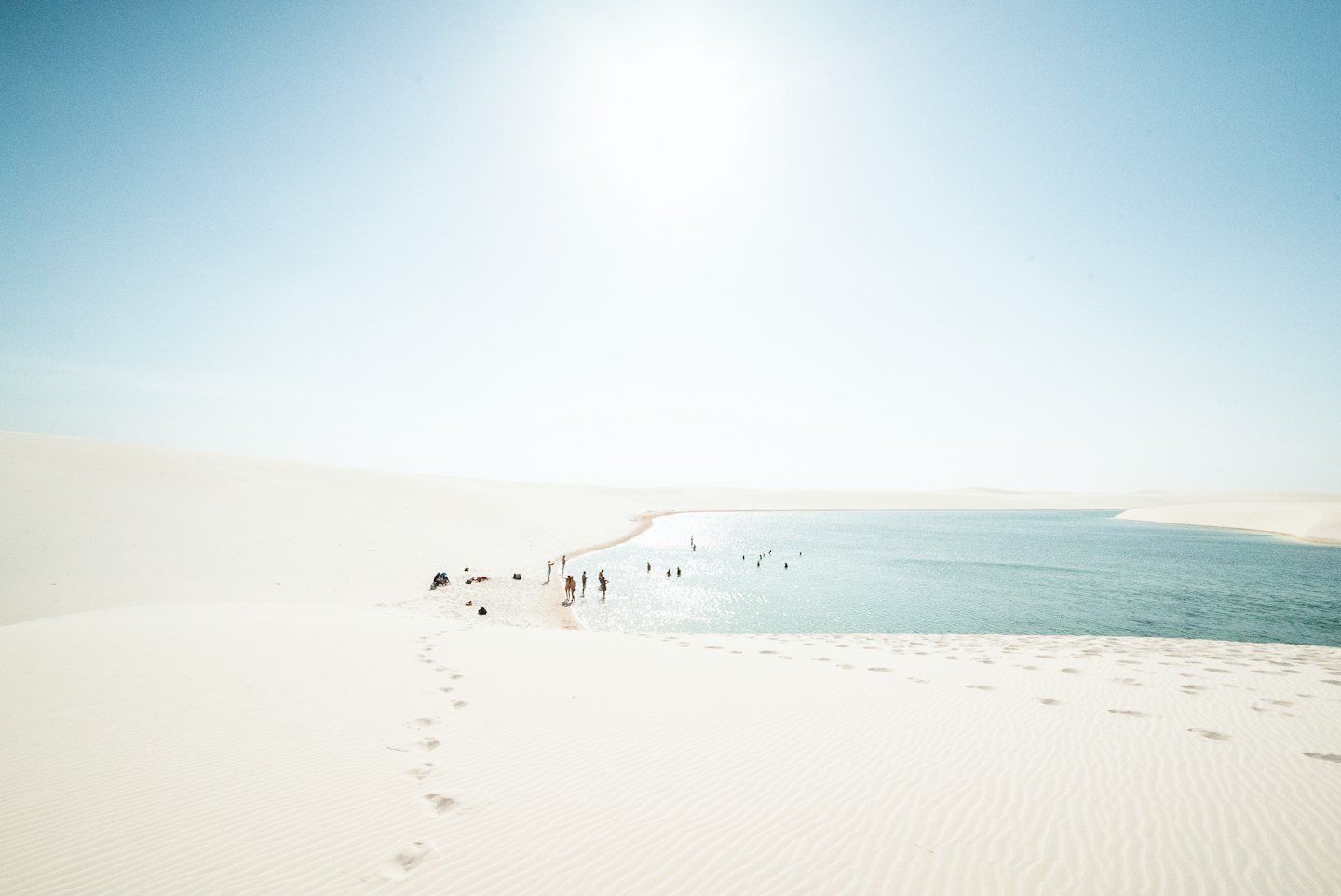 People wading in a blue lagoon surrounded by white sand dunes.