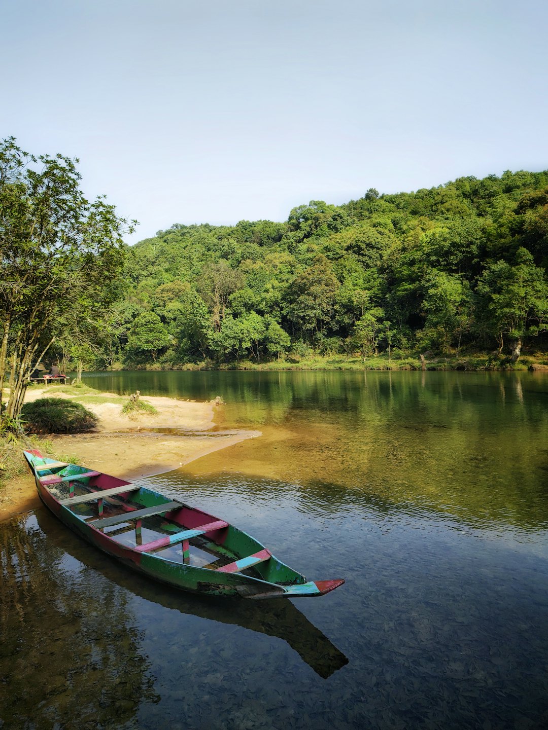 A multicolored canoe rests on a sandy riverbank.